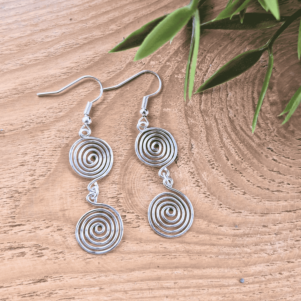 Silver spiral earrings on a wooden surface with green leaves.