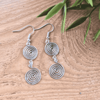 Silver spiral earrings on a wooden surface with green leaves.