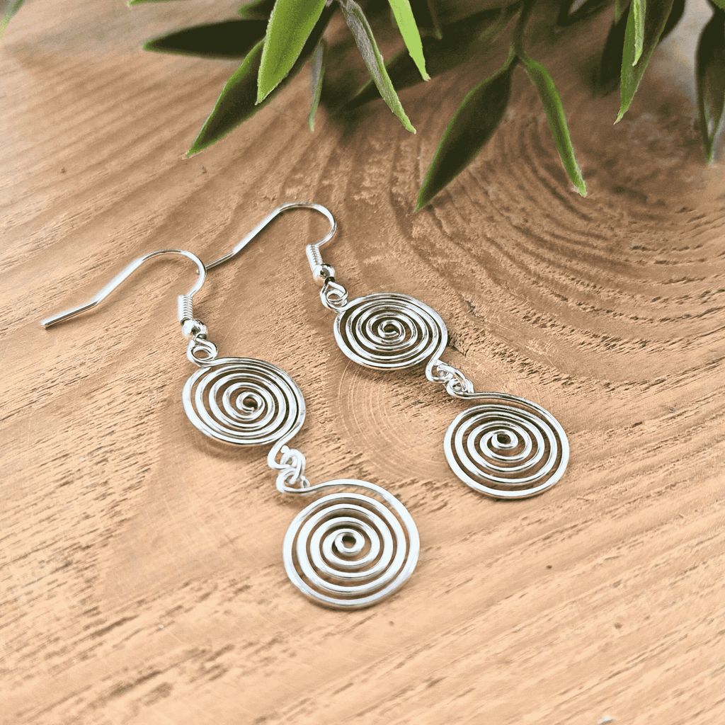 Silver spiral earrings on a wooden surface with green leaves in the background