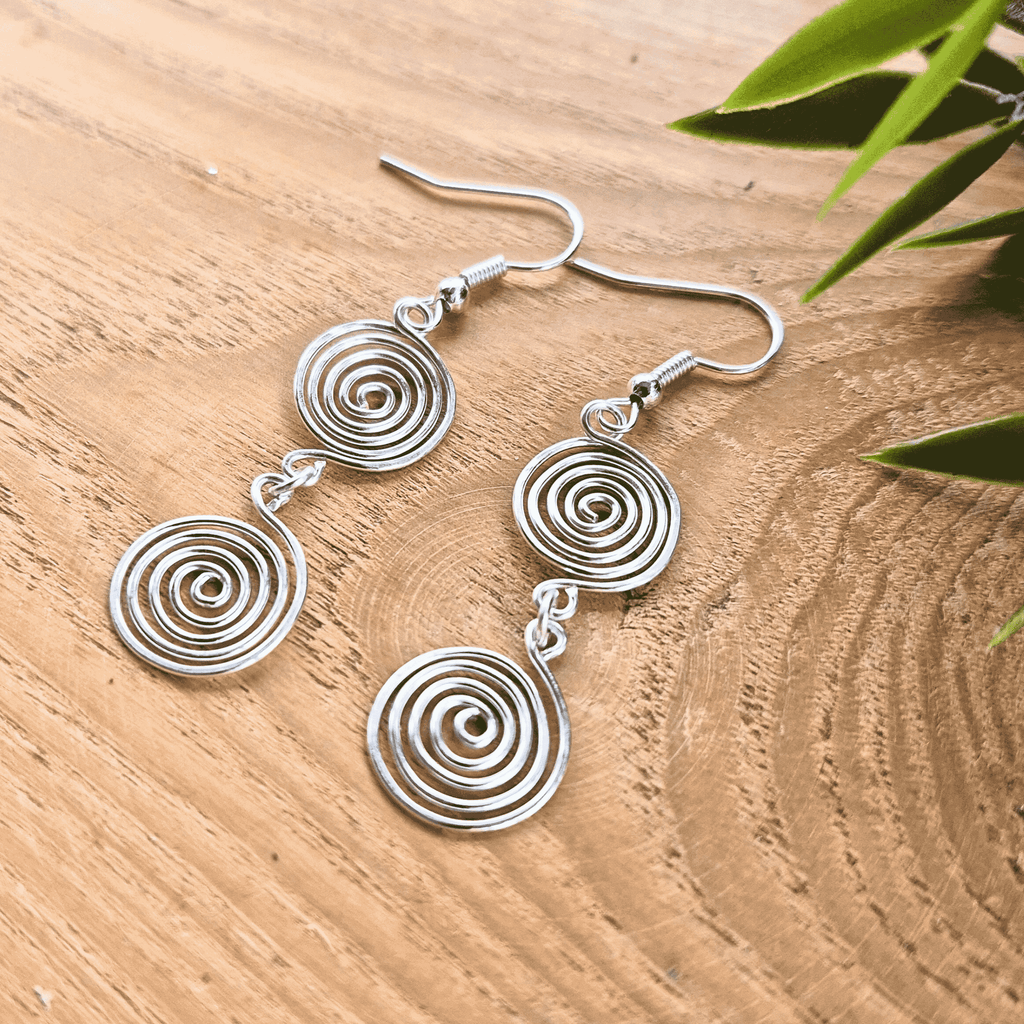 Silver spiral earrings on a wooden surface with green leaves.