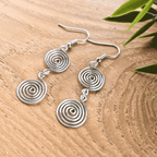 Silver spiral earrings on a wooden surface with green leaves.
