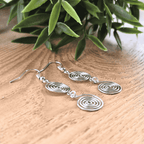 Silver spiral earrings on a wooden surface with green leaves in the background
