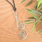 Silver spiral pendant on a black cord with green leaves on a wooden surface