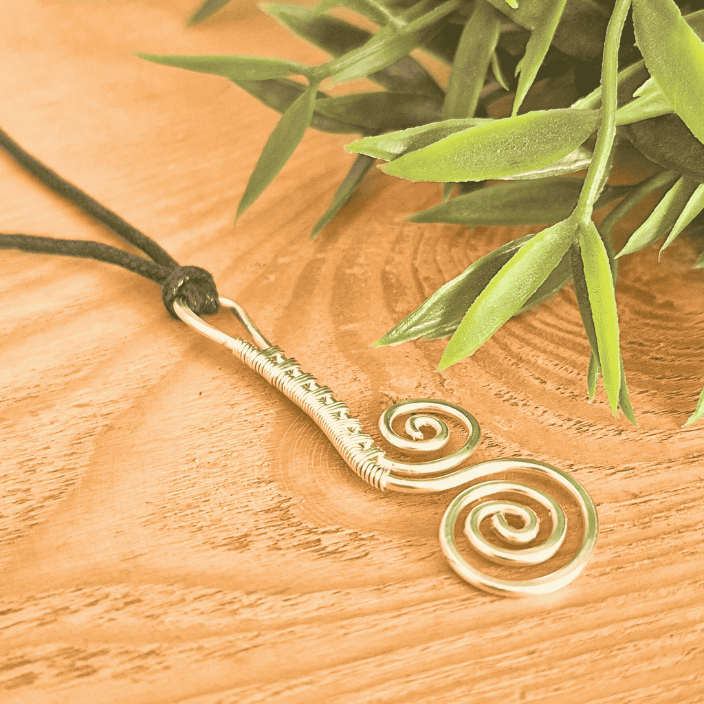 Gold spiral pendant necklace on a wooden surface with green leaves