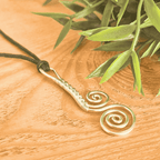 Gold spiral pendant necklace on a wooden surface with green leaves