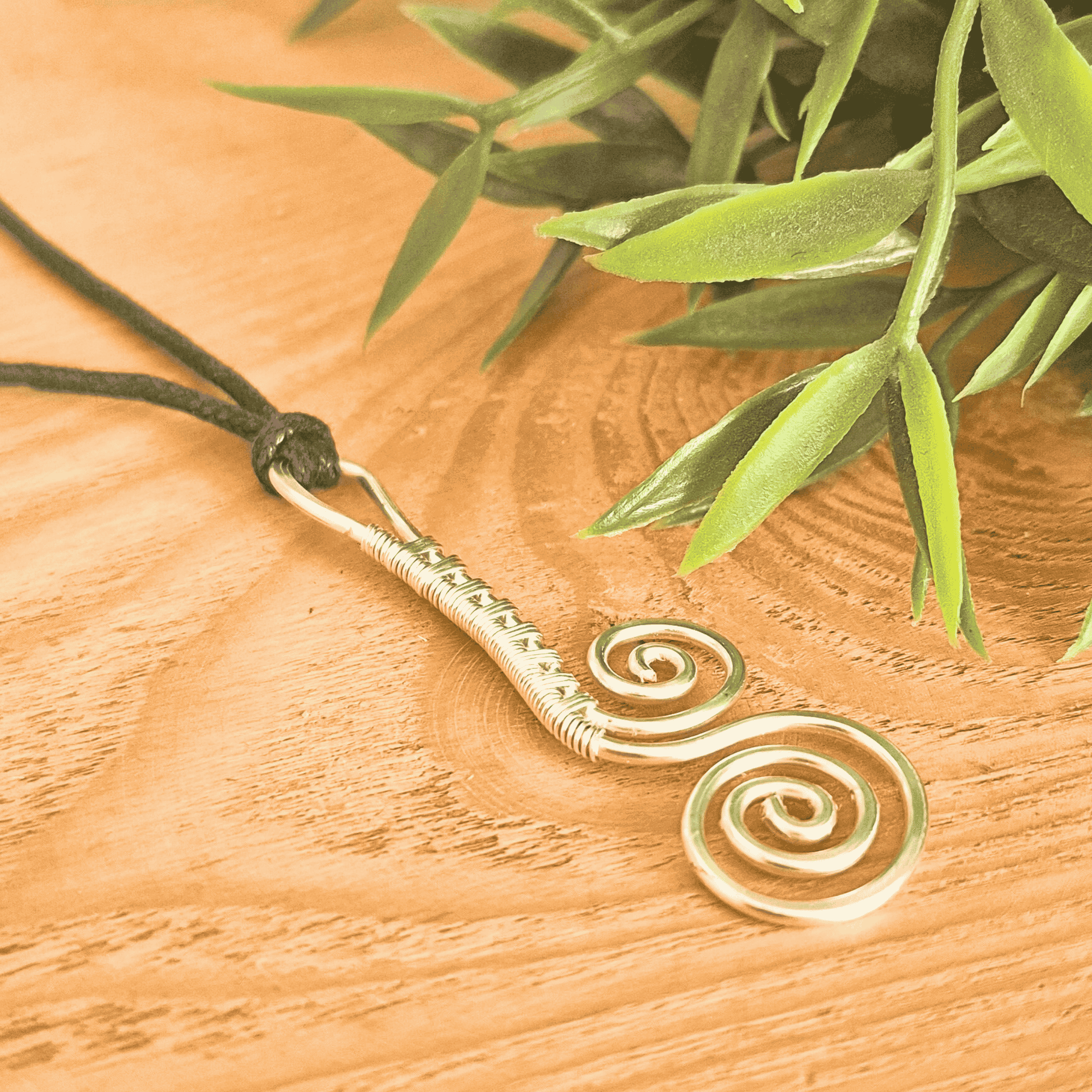 Gold spiral pendant necklace on a wooden surface with green leaves