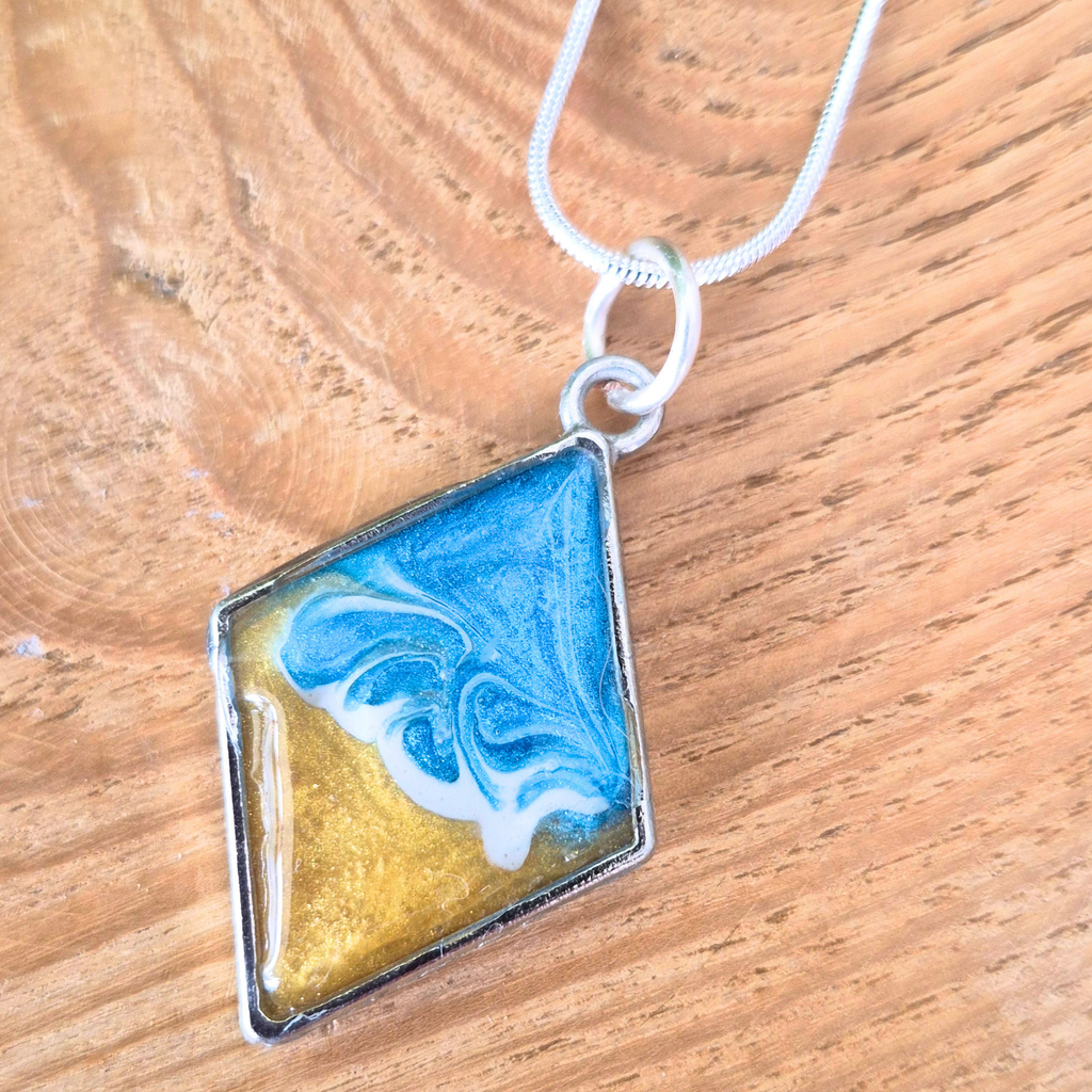 Silver bezel pendant with a wave effect centre on a silver chain on a wooden surface