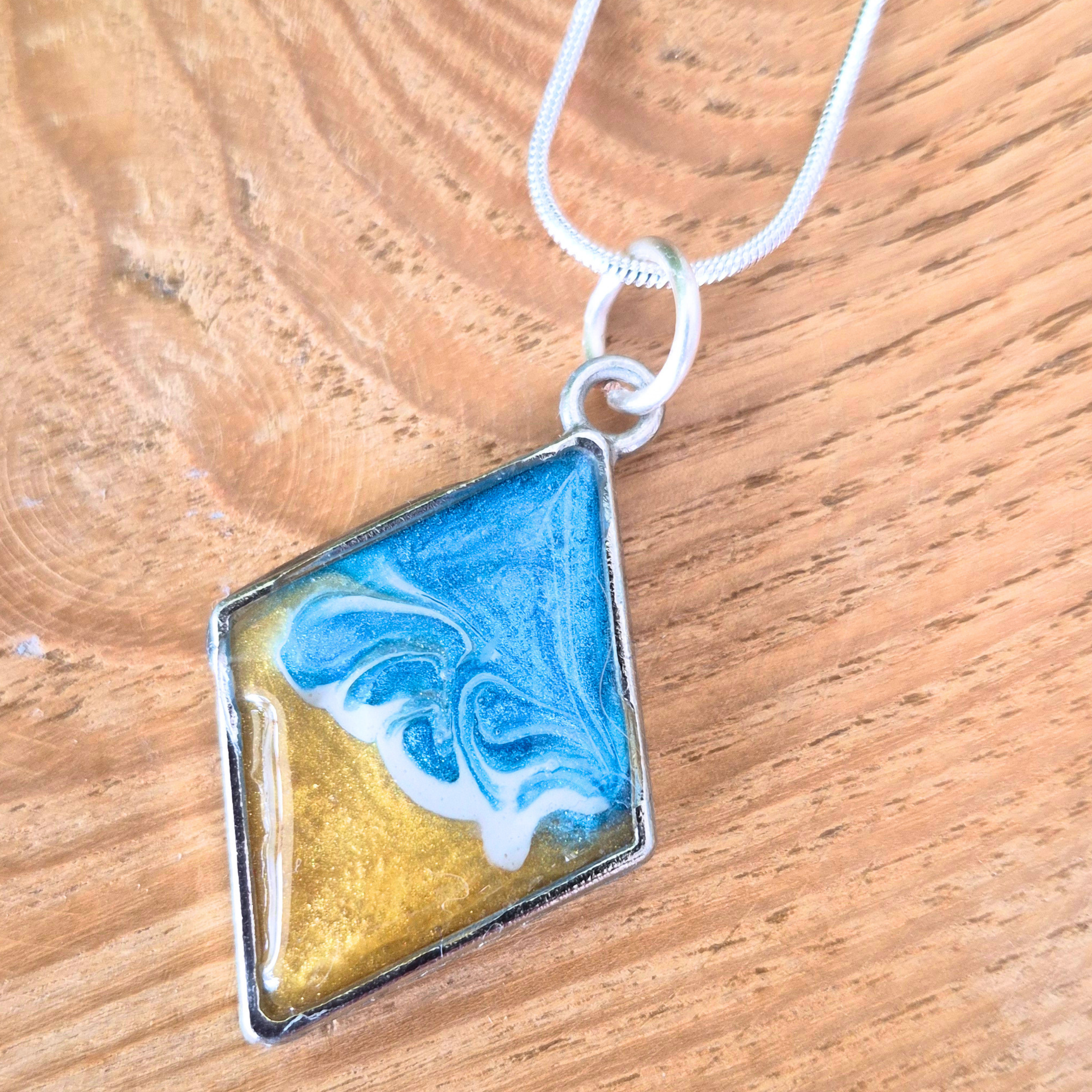 Silver bezel pendant with a wave effect centre on a silver chain on a wooden surface