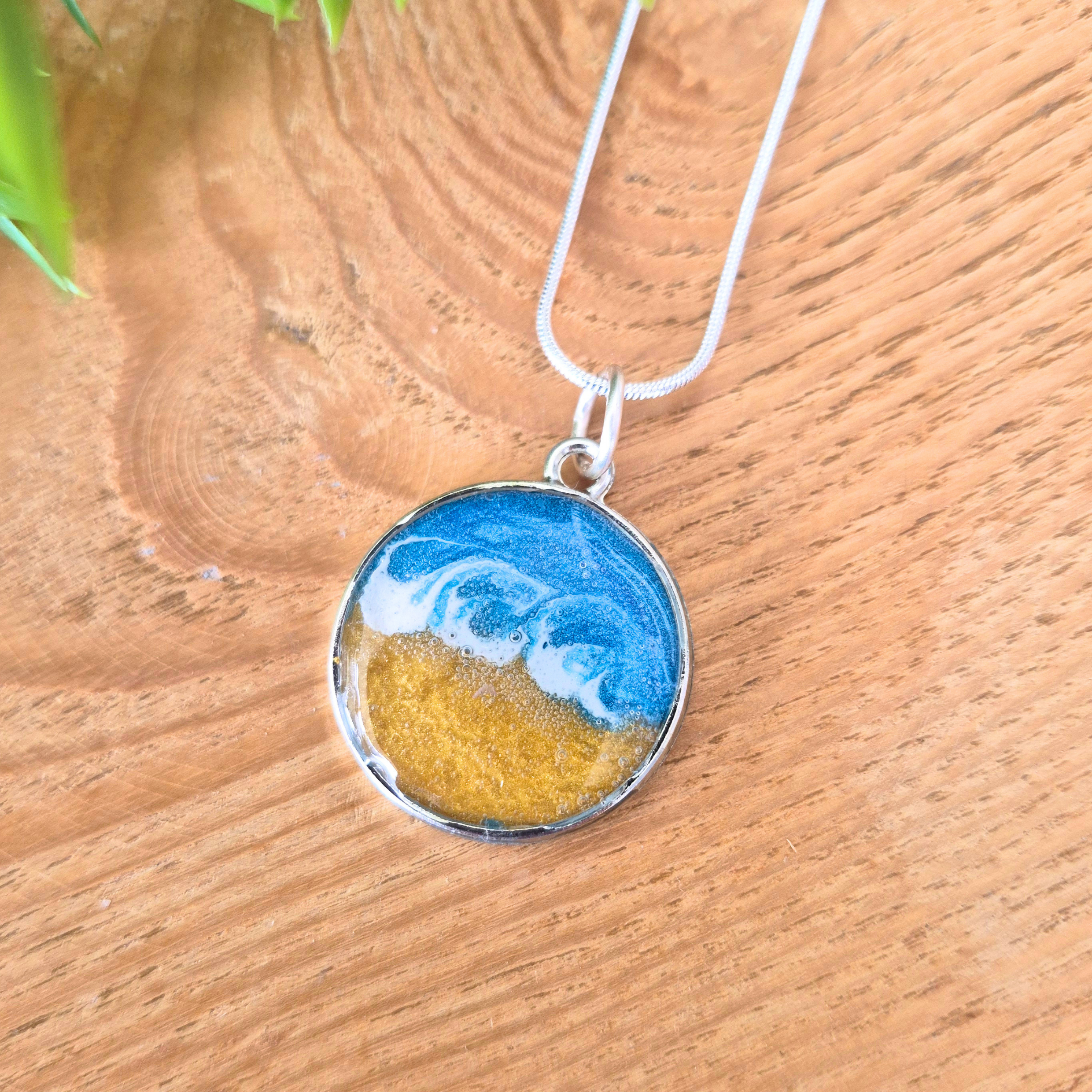Necklace with a round pendant featuring blue and yellow design on a wooden surface