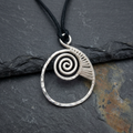 Silver spiral pendant on a black cord against a dark stone background