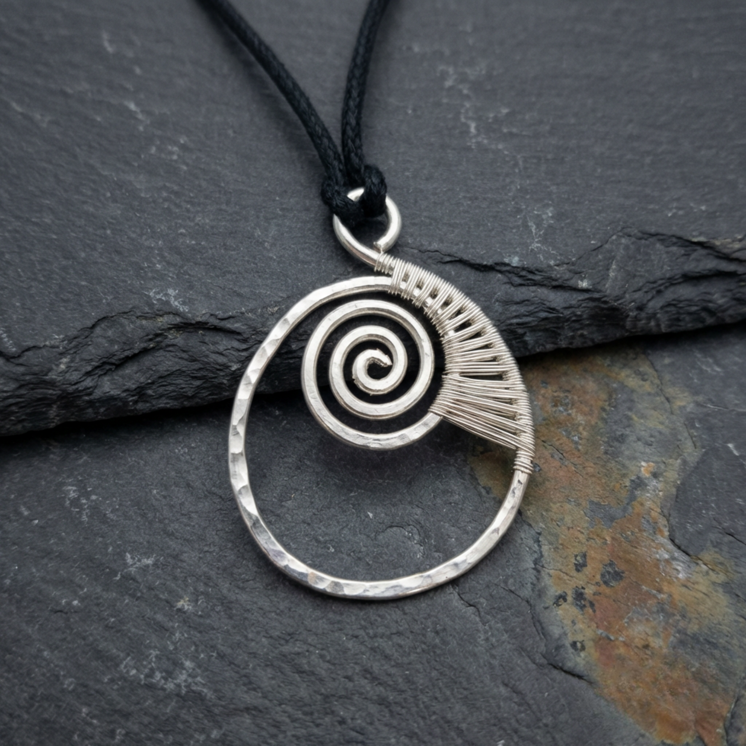 Silver spiral pendant on a black cord against a dark stone background
