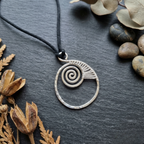Silver spiral pendant necklace on a dark surface with dried plants and stones.