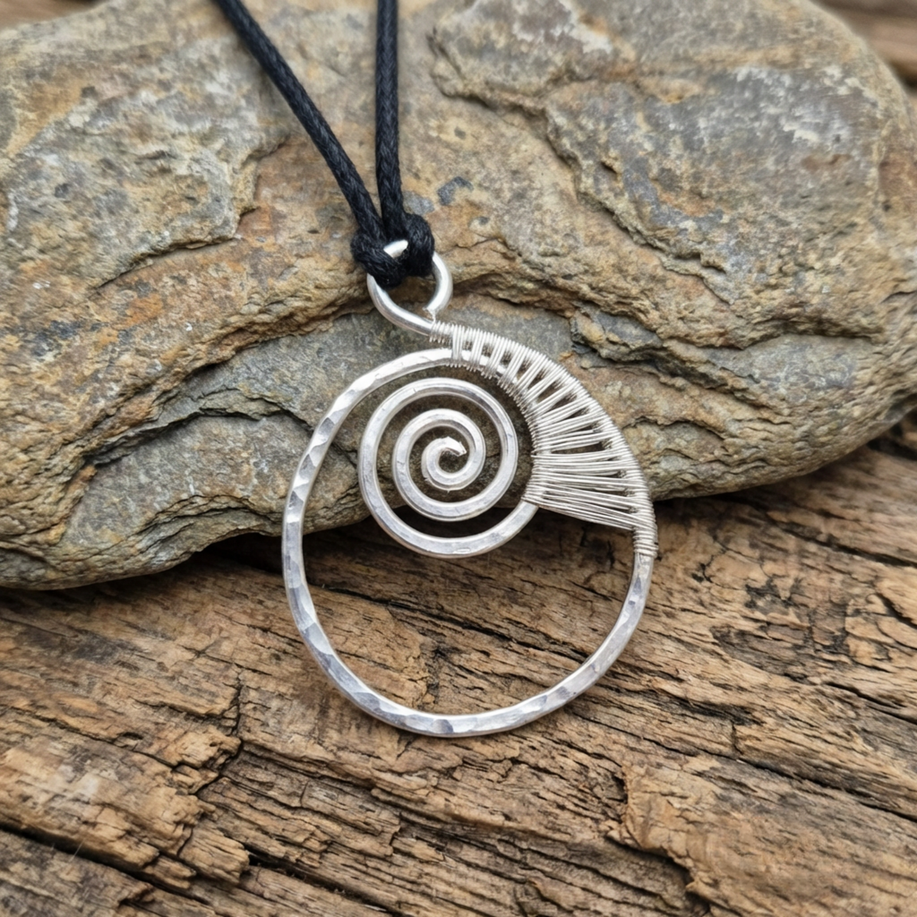 Ammonite fossil silver spiral pendant on a wood and stone surface