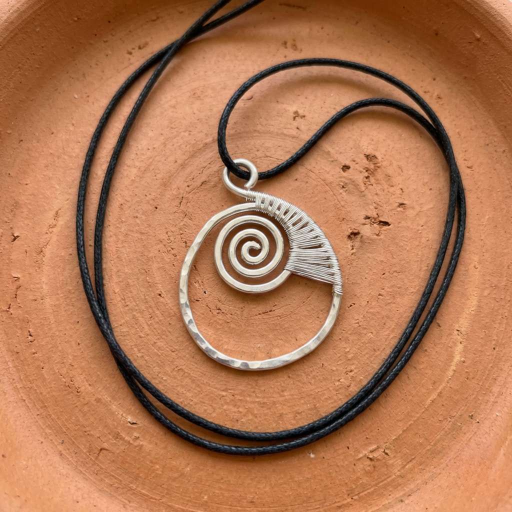 Silver spiral pendant on black cord against a terracotta background