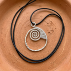 Silver spiral pendant on black cord against a terracotta background