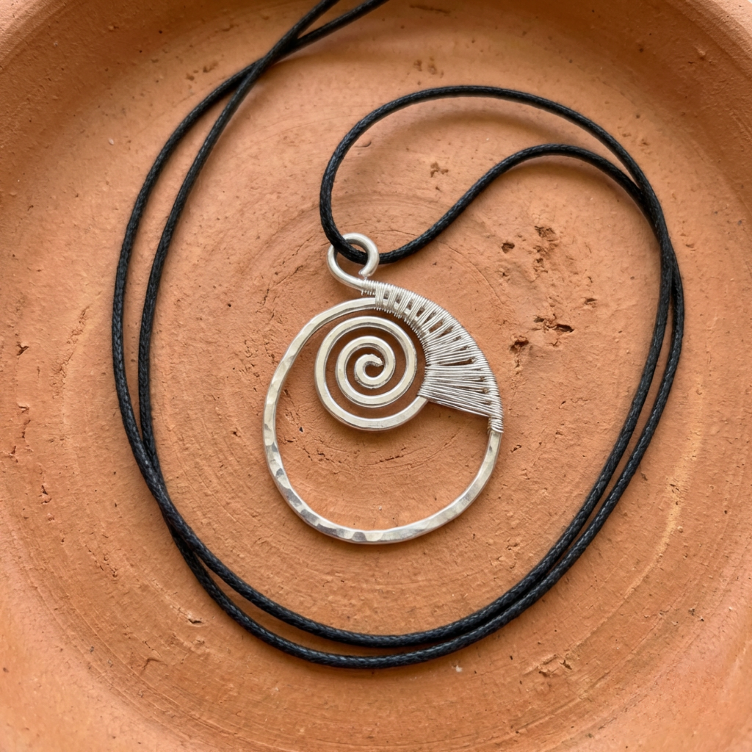Silver spiral pendant on black cord against a terracotta background