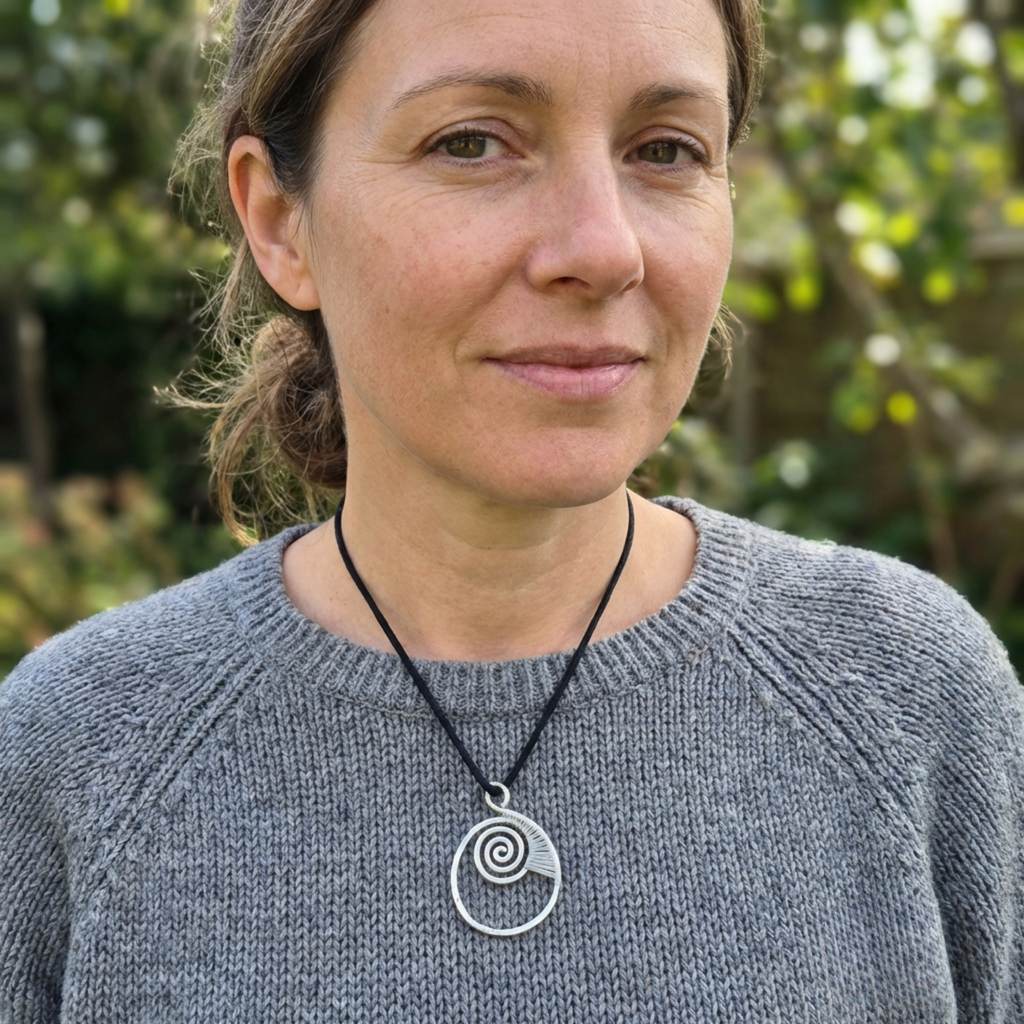 Woman wearing a gray sweater with a necklace featuring a silver spiral pendant, outdoors.