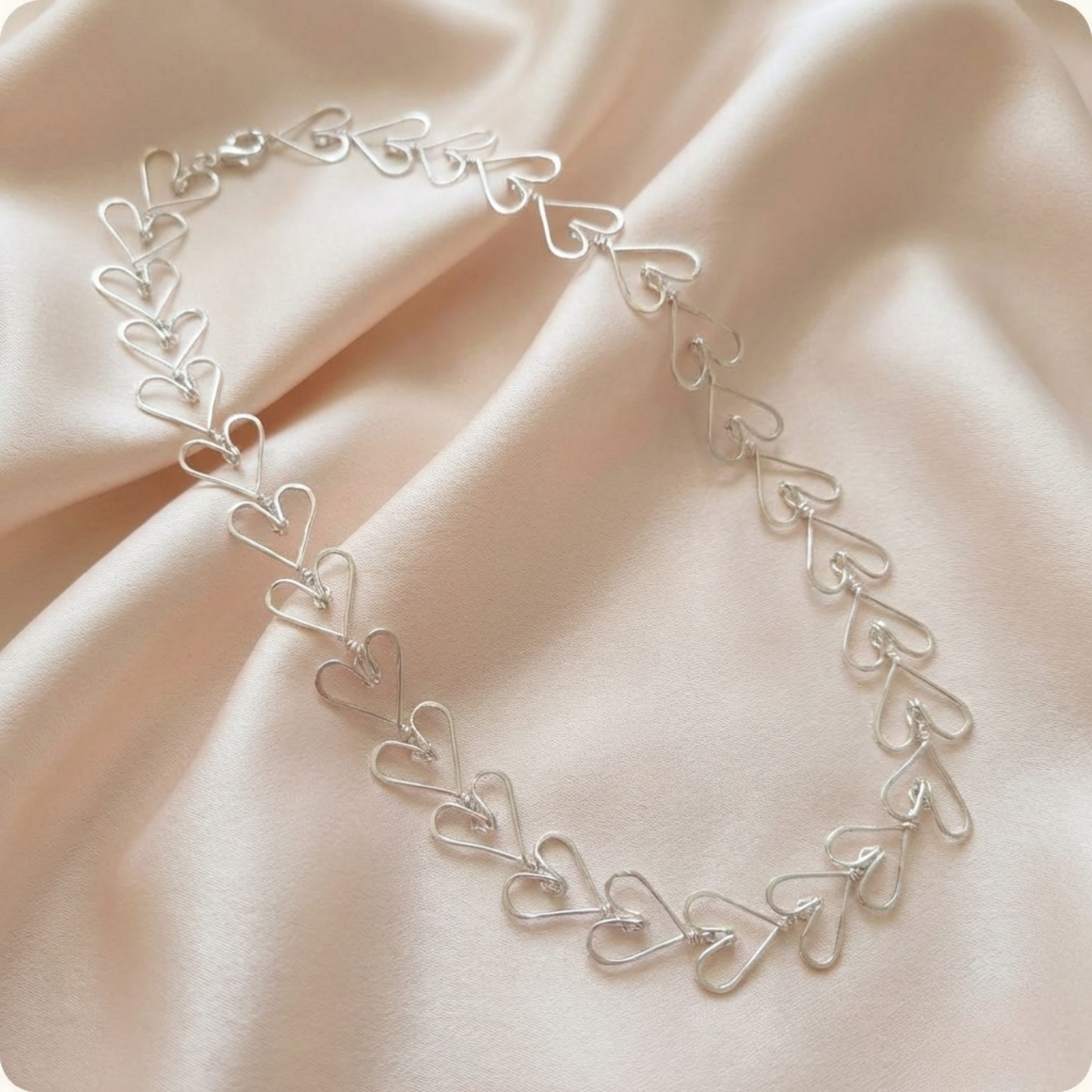 Silver heart-shaped necklace on a soft pink fabric background