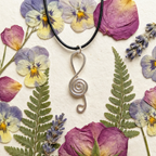 Silver spiral pendant necklace on a background of pressed flowers and leaves