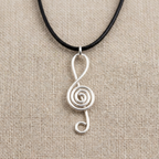 Silver treble clef pendant on a black cord against a beige fabric background