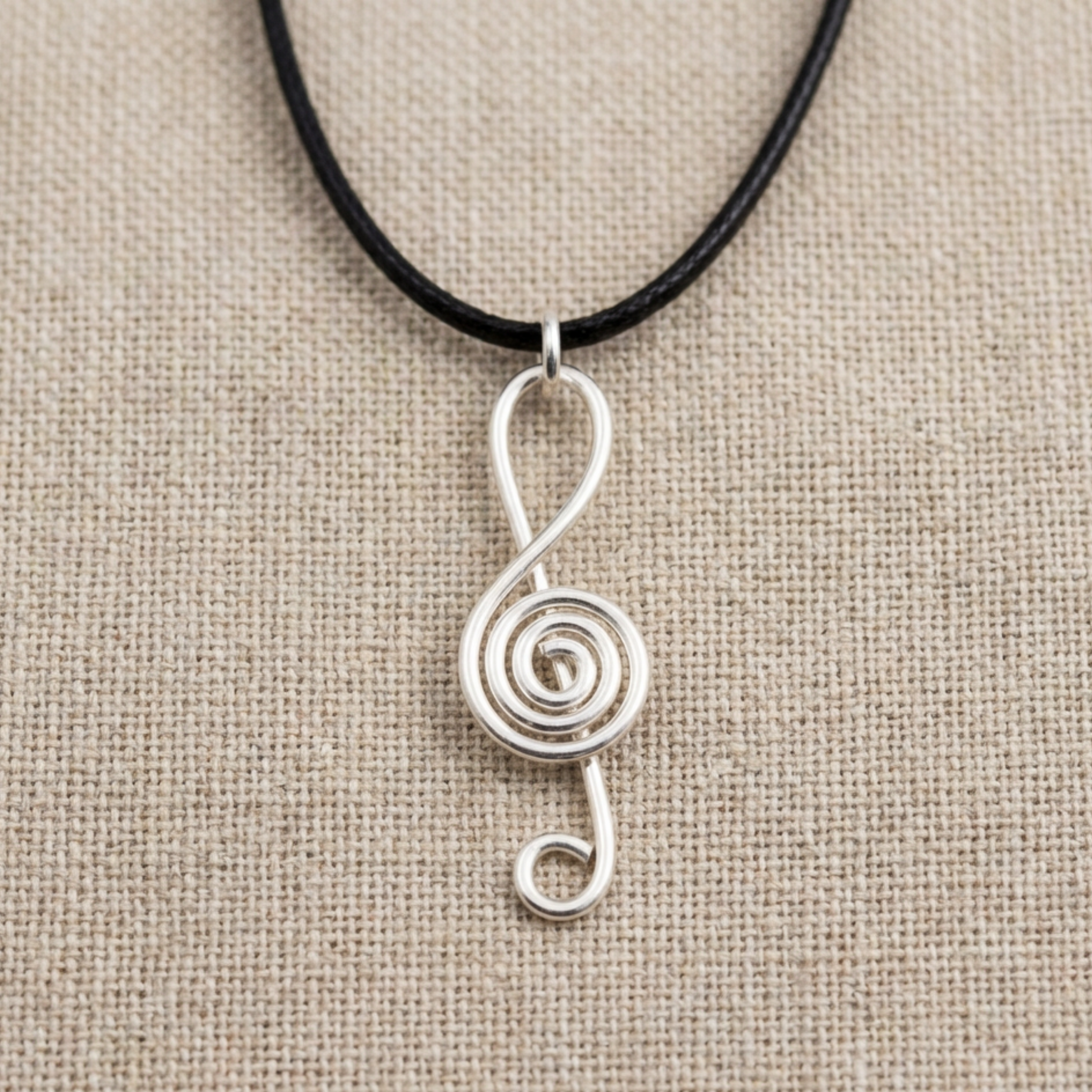 Silver treble clef pendant on a black cord against a beige fabric background
