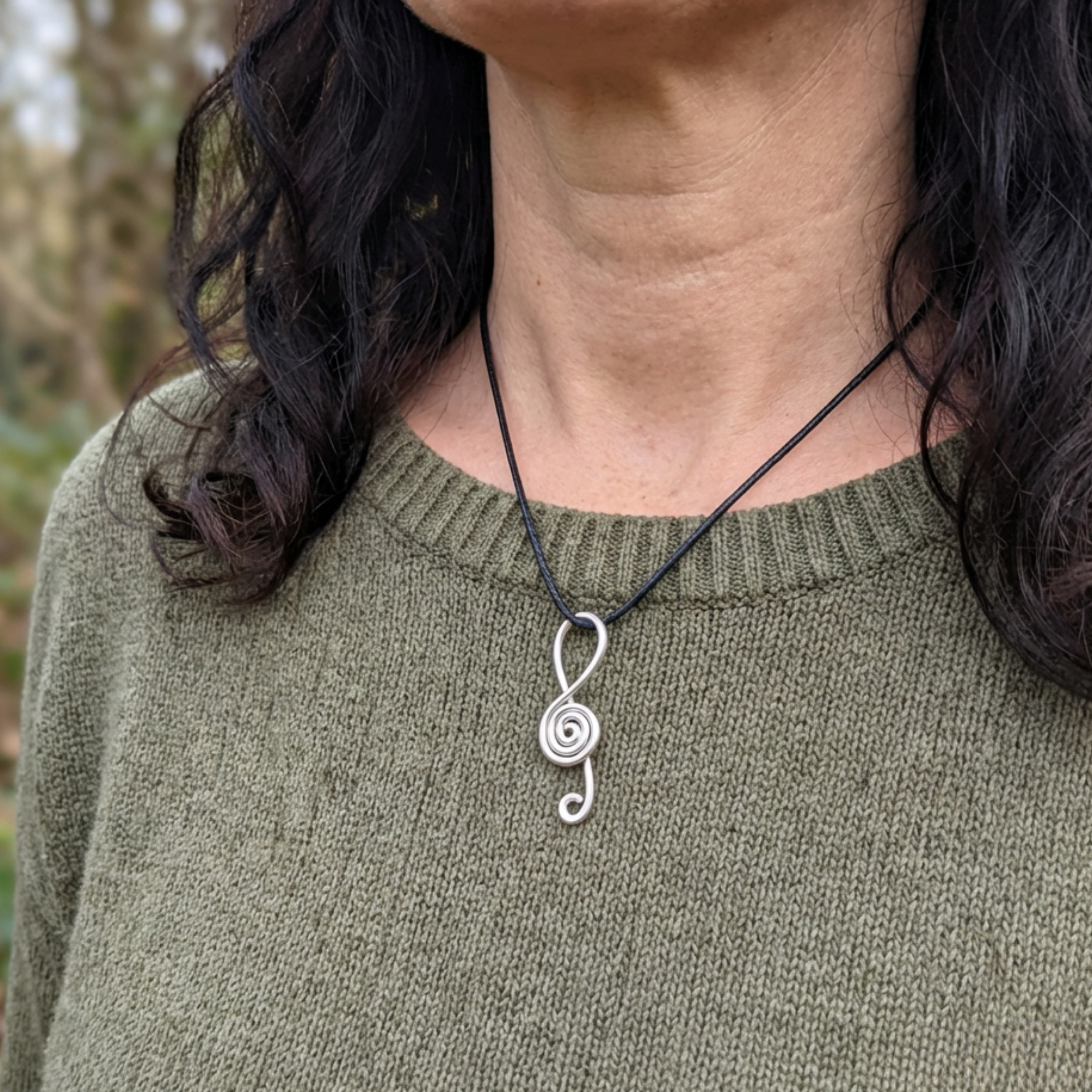 Person wearing a green sweater with a silver necklace featuring a unique pendant.
