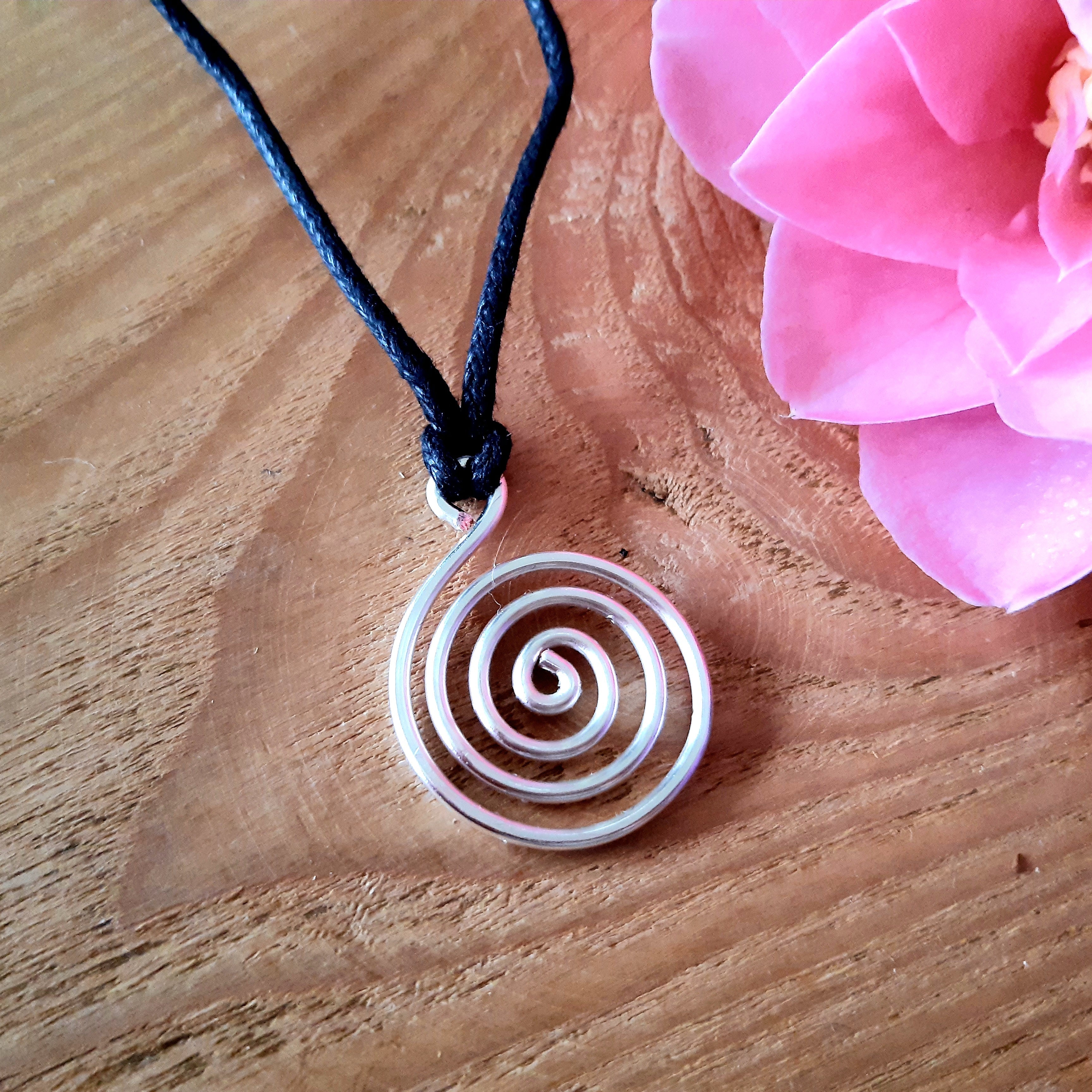 Spiral pendant necklace on a wooden surface with a pink flower in the background