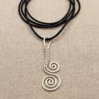 Silver spiral pendant on a black cord against a beige fabric background