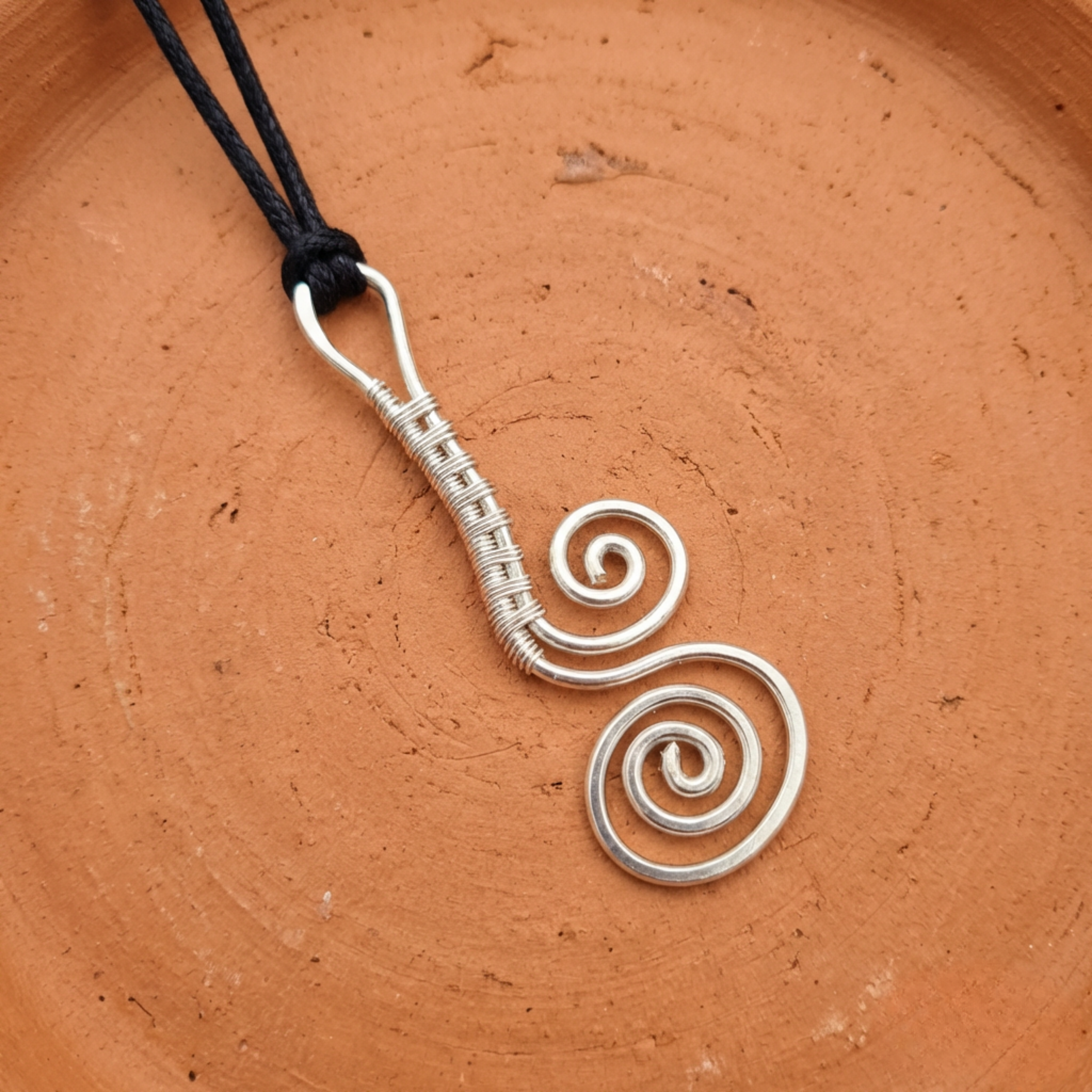 Silver spiral pendant on a black cord against a terracotta background