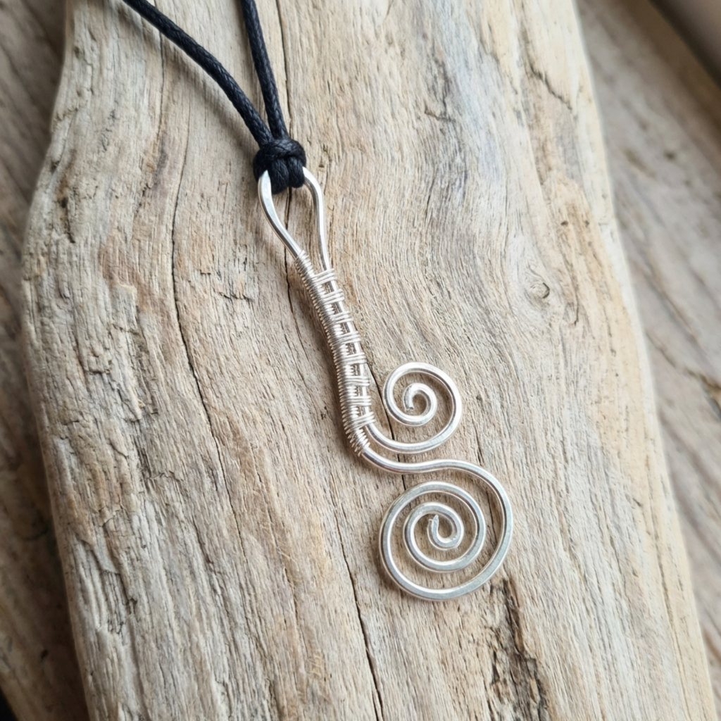 Silver spiral pendant on a black cord against a wooden background