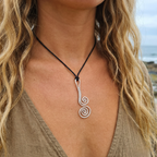 Person wearing a silver spiral pendant necklace with a blurred natural background