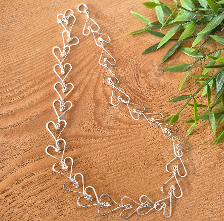 Silver heart-shaped necklace on a wooden surface with green leaves