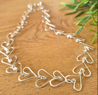 Silver heart-shaped necklace on a wooden surface with green leaves.