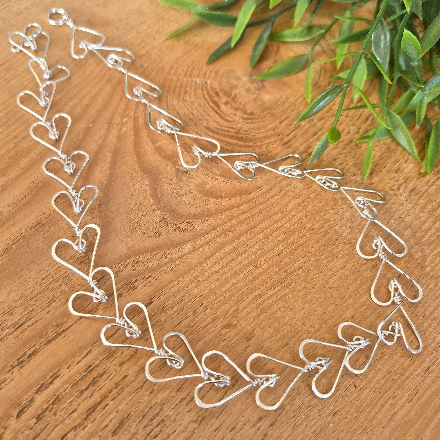 Silver heart-shaped necklace on a wooden surface with green leaves in the background