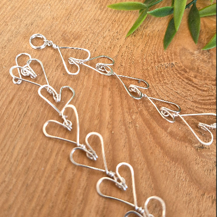 Silver heart-shapes necklace on a wooden surface with green leaves.