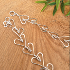 Silver heart-shapes necklace on a wooden surface with green leaves.