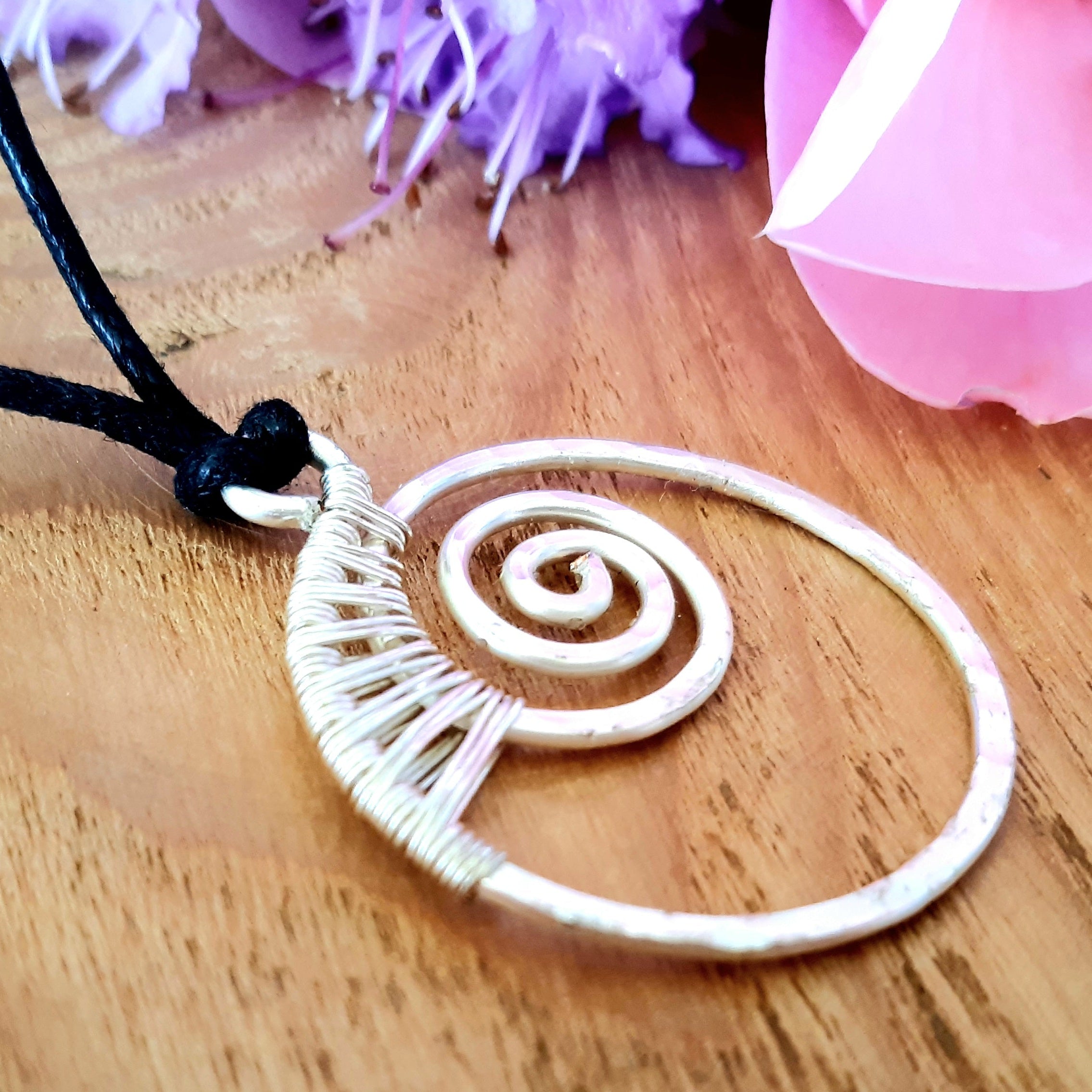 White spiral pendant on a black cord with pink flowers in the background