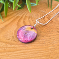A small round resin pendant with pinks purples and gold spiralling on a wooden surface