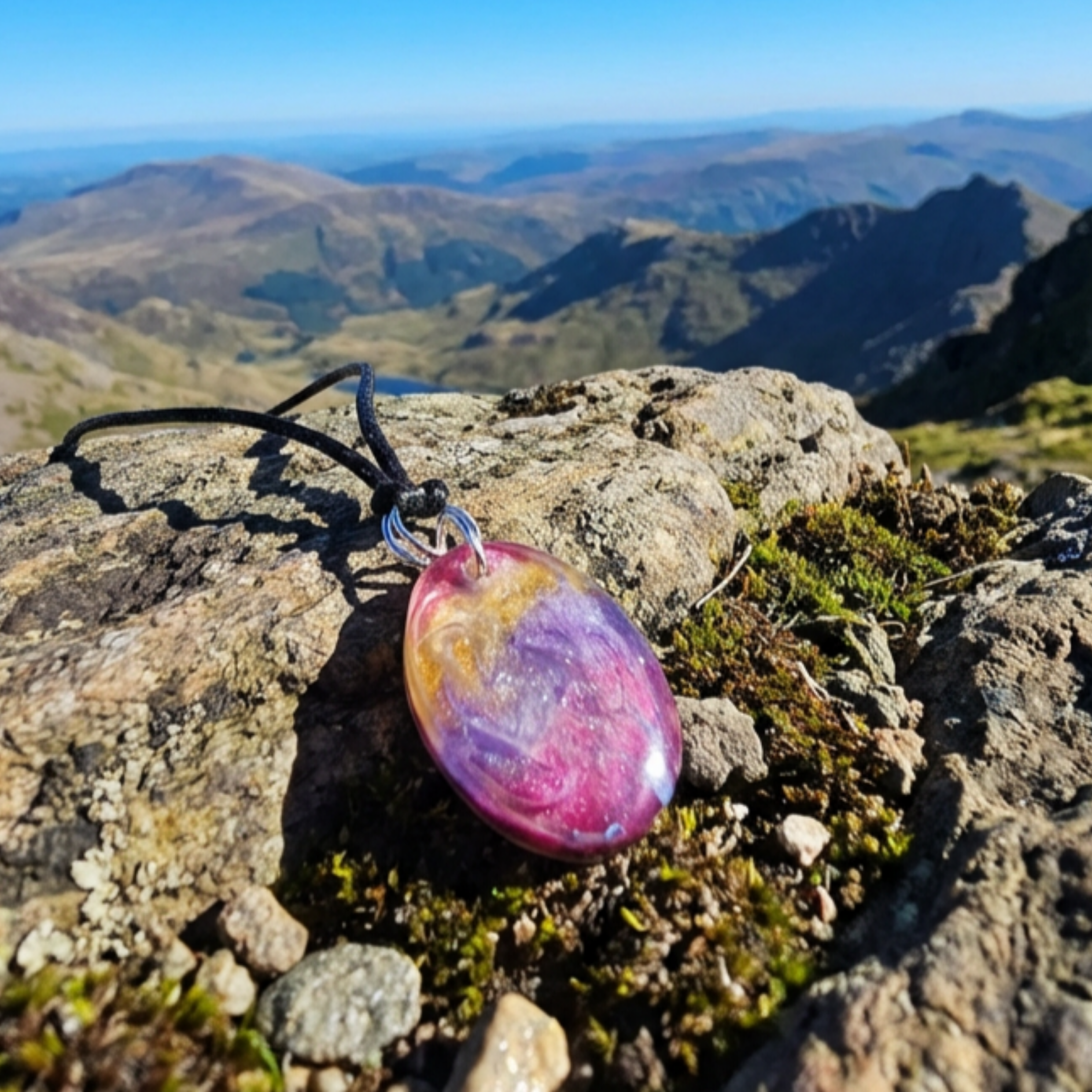 Multicolored pendant on a chain on a rocky mountain top with a scenic view.