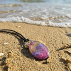Small oval resin pendant with pink gold and purple colouring on the beach