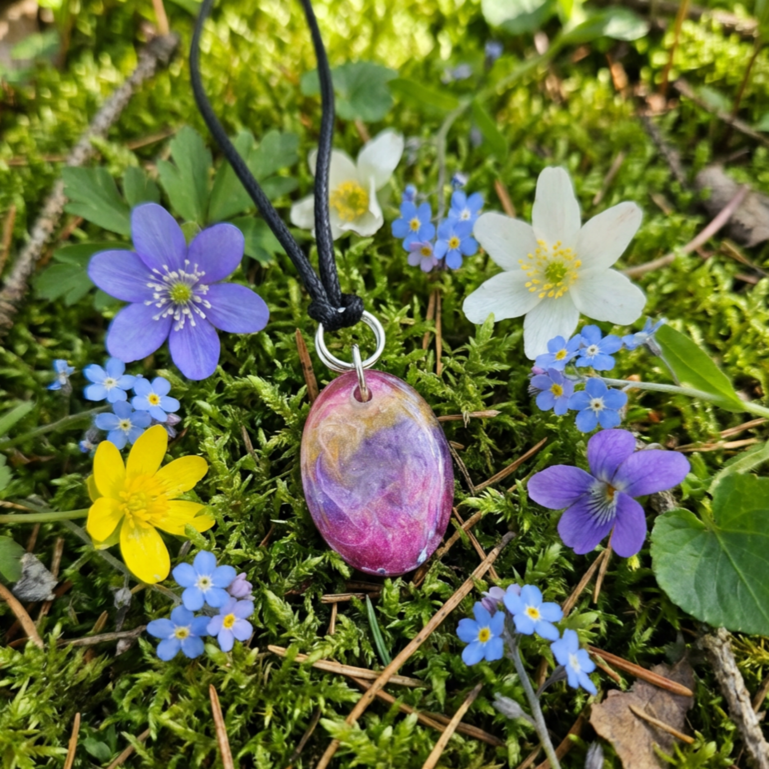 Colourful oval pendant on moss surrounded with flowers