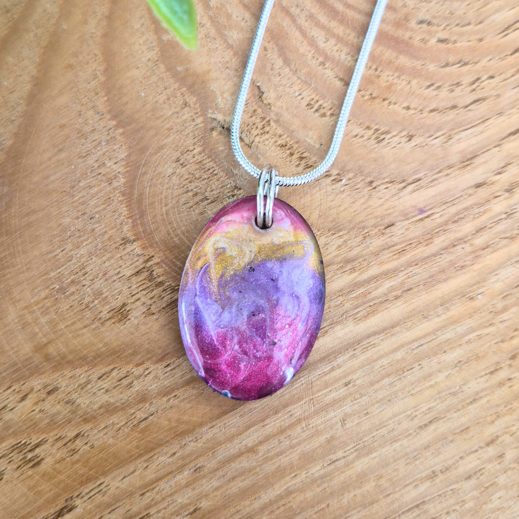 Oval-shaped purple and gold pendant on a wooden surface