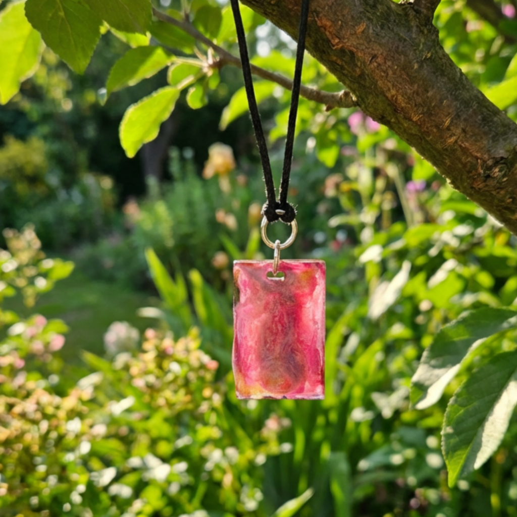 Pink pendant on a cord hanging from a tree branch with green leaves in the background