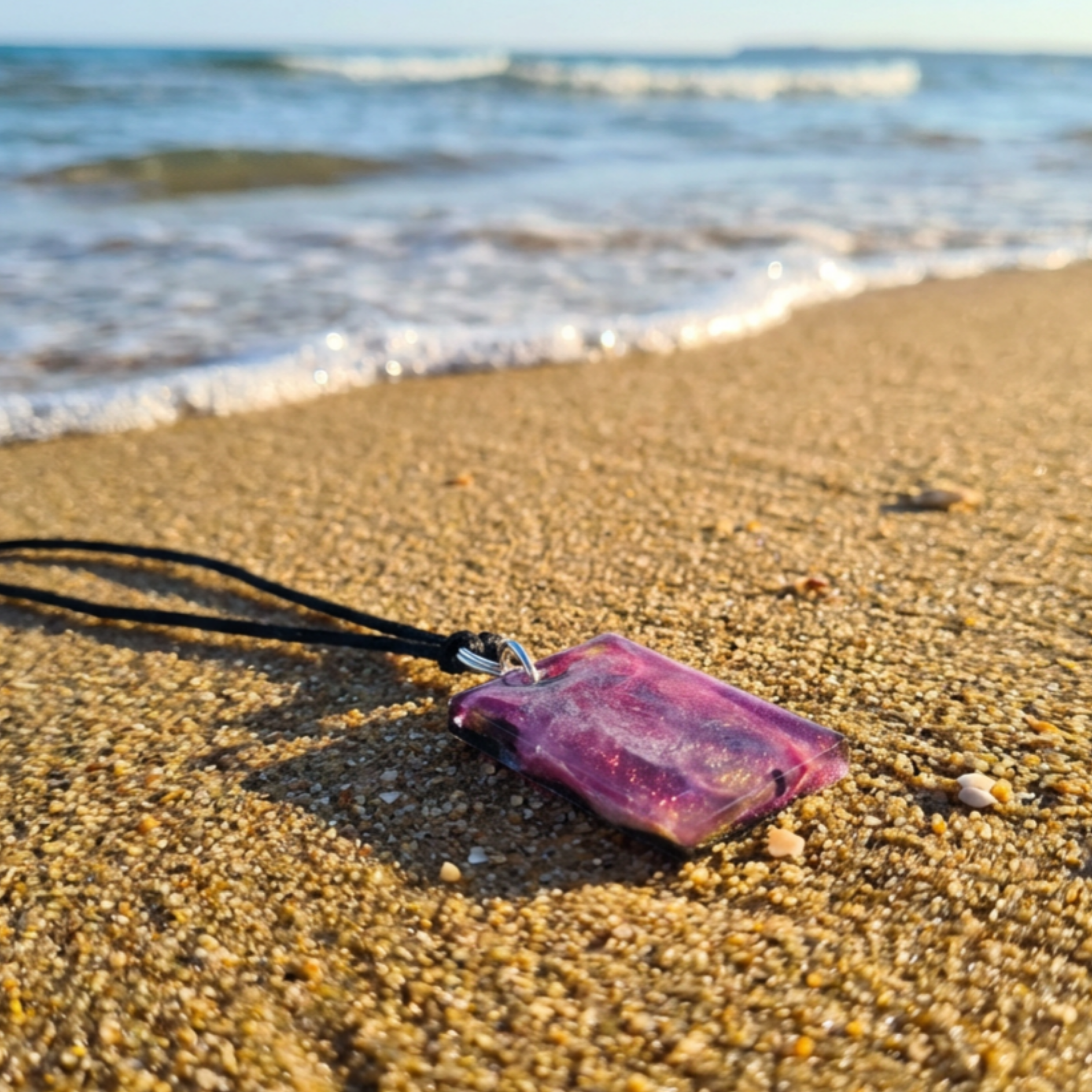 Rectangle pink gold purple pendant with a black back made from uv resin on a beach