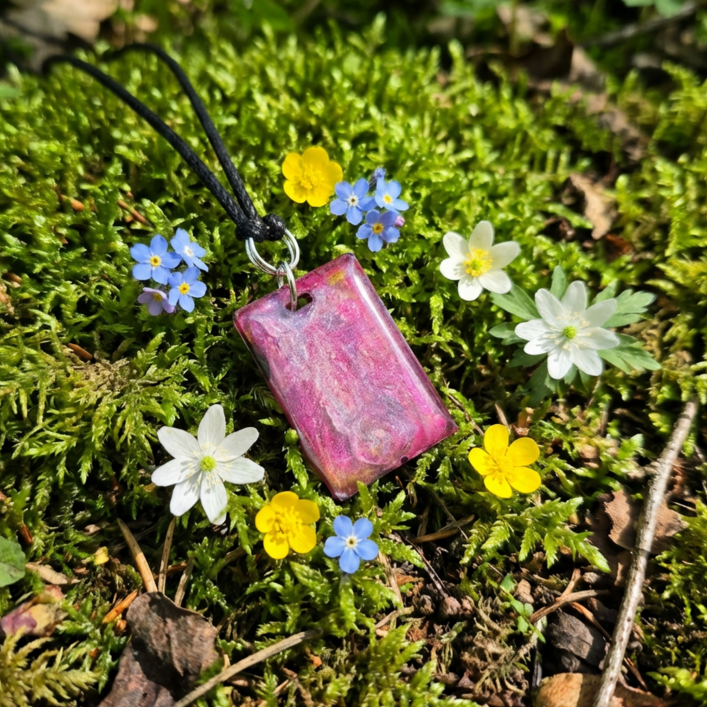 Pink pendant on a black cord surrounded by small flowers on green moss
