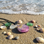 Round pink purple gold pendant on sand with shells