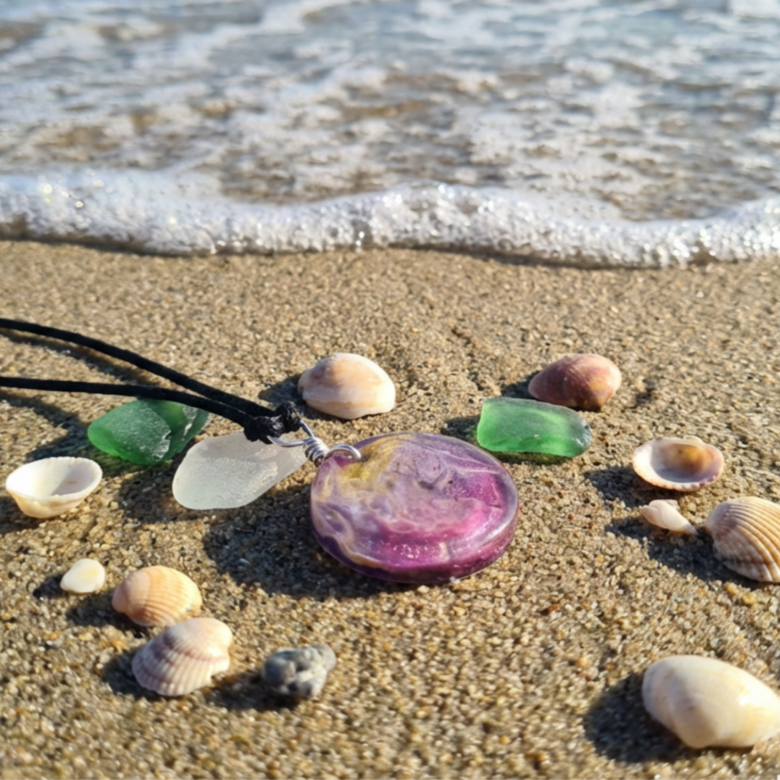 Round pink purple gold pendant on sand with shells