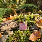 Necklace with a square pendant on a forest floor with moss, leaves, and rocks.