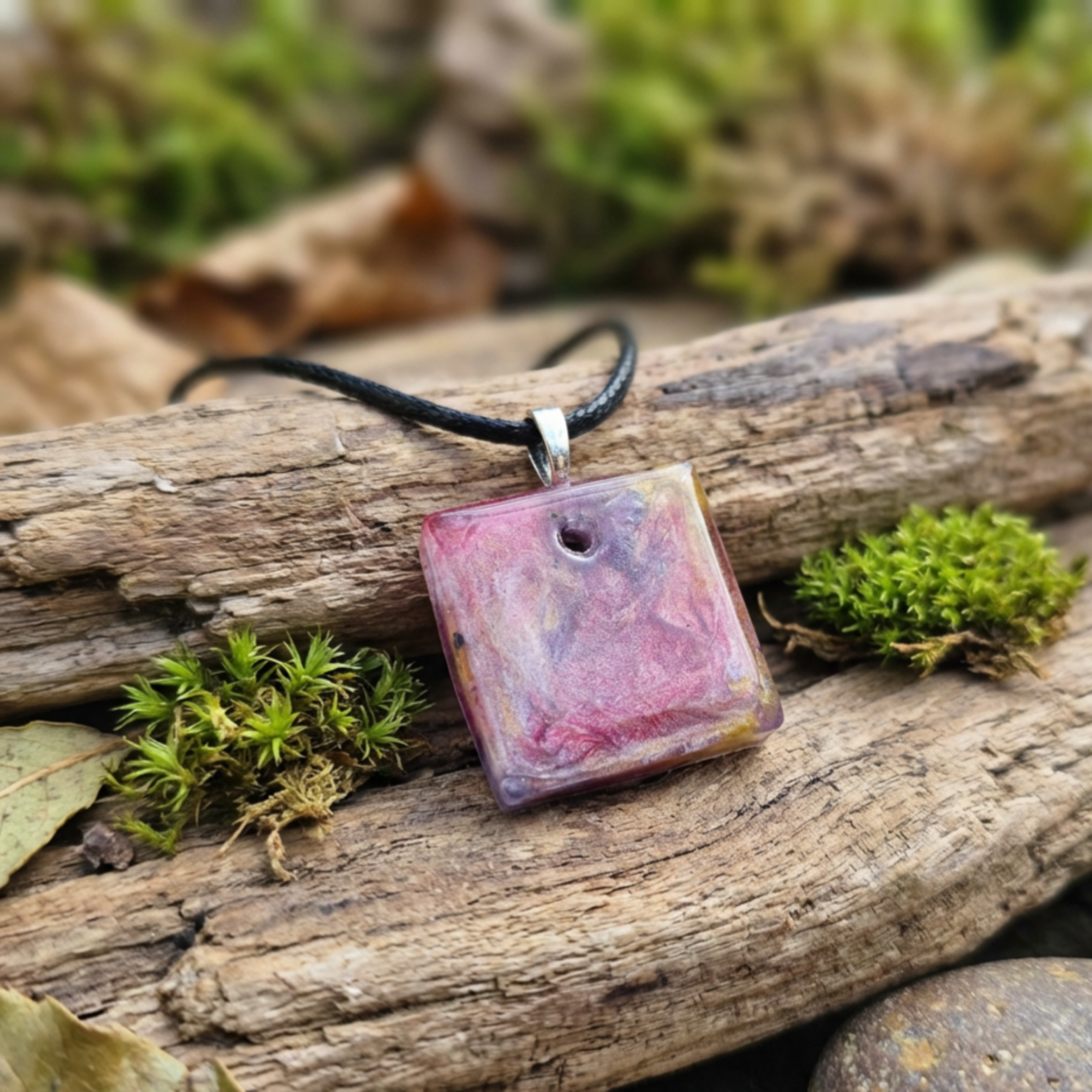 Necklace with a square, multicolored pendant on a wooden log with moss