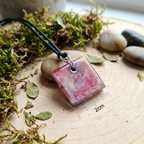 Square pink pendant on a string with a ruler for scale, surrounded by nature-themed elements.